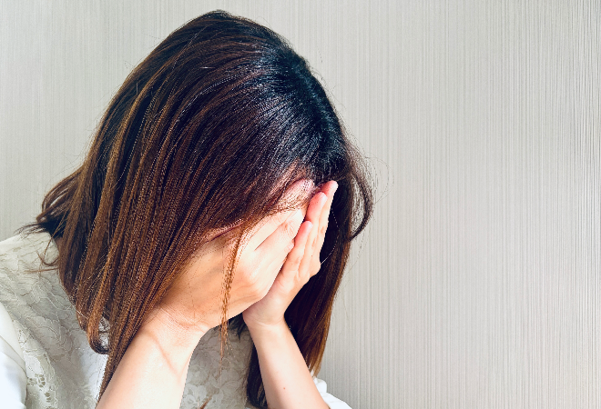 顏を手で覆い、泣いている女性の横顔。