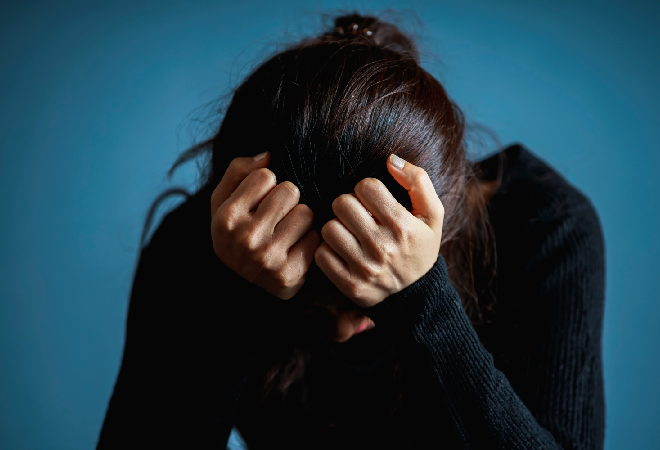 膝を抱え落ち込む中年女性。