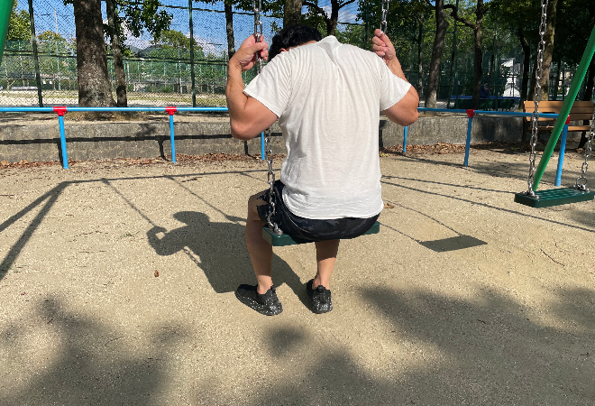 ブランコに乗り落ち込む様子の男性。
