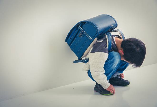廊下でしゃがみ込むランドセル姿の小学生男子。