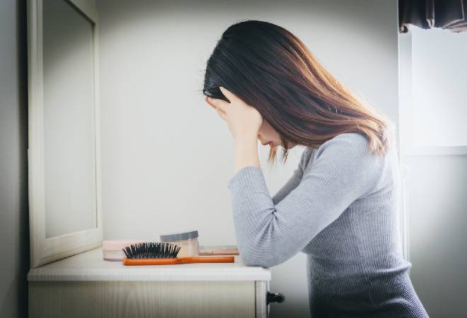 化粧台の前で頭を抱える女性の横顔。