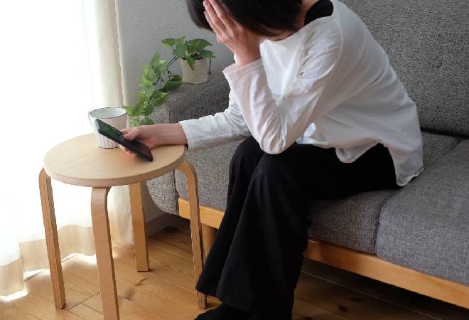 スマホを持ち頭を抱える母親。