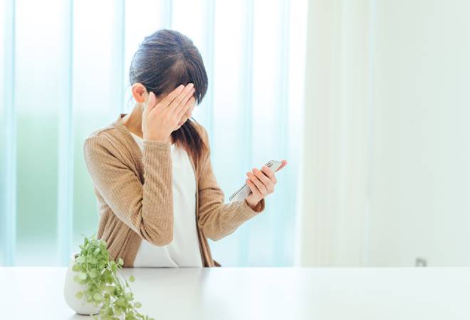 スマートフォンを見てショックを受ける女性の姿。
